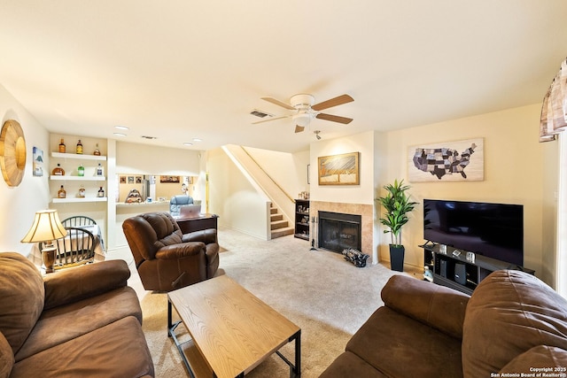 living area featuring a fireplace, light colored carpet, visible vents, a ceiling fan, and stairs