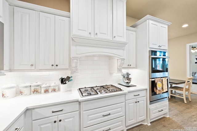 kitchen featuring light wood-style flooring, white cabinets, light countertops, appliances with stainless steel finishes, and tasteful backsplash