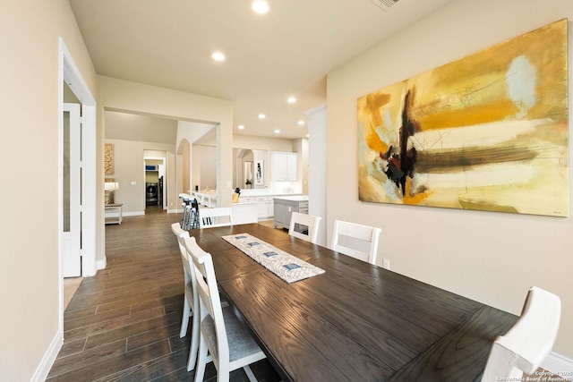 dining space with dark wood-style floors, recessed lighting, arched walkways, and baseboards