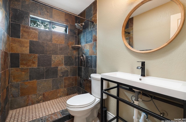 full bath featuring a textured wall, a sink, a tile shower, and toilet