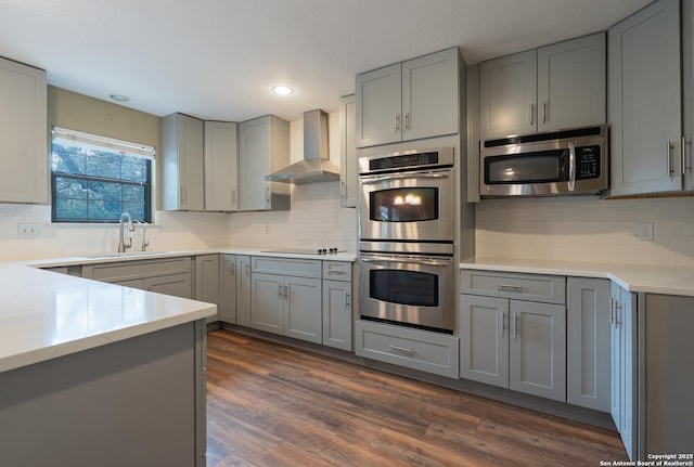 kitchen with wall chimney exhaust hood, gray cabinets, stainless steel appliances, light countertops, and a sink