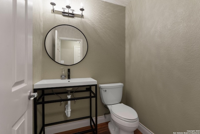 bathroom featuring a textured wall, toilet, a sink, wood finished floors, and baseboards