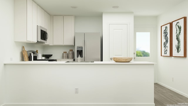 kitchen with appliances with stainless steel finishes, wood finished floors, a peninsula, light countertops, and white cabinetry