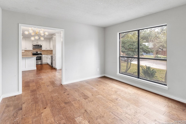 interior space with light wood-type flooring, baseboards, a chandelier, and a textured ceiling