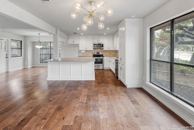 kitchen with light stone counters, wood finished floors, white cabinets, appliances with stainless steel finishes, and pendant lighting