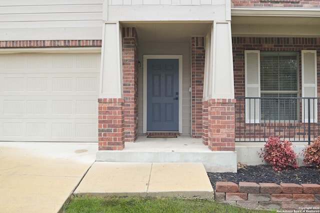 view of exterior entry with an attached garage and brick siding