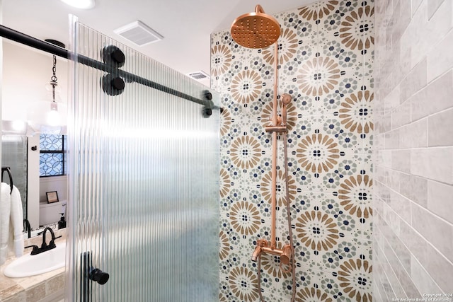 full bath featuring tiled shower, a sink, and visible vents