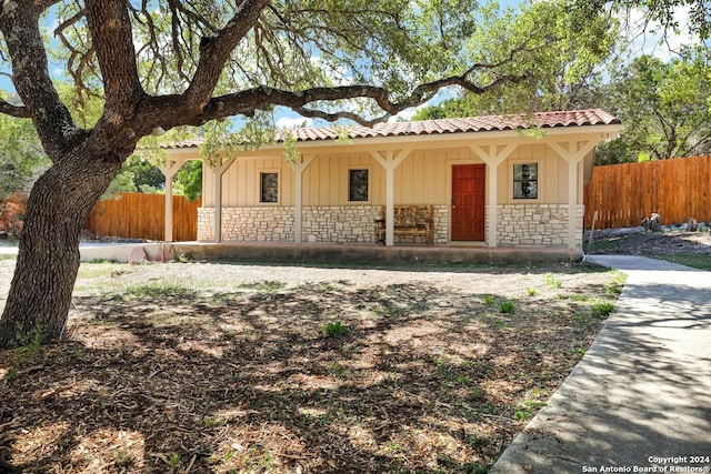 mediterranean / spanish-style house featuring stone siding, fence, board and batten siding, and a tiled roof