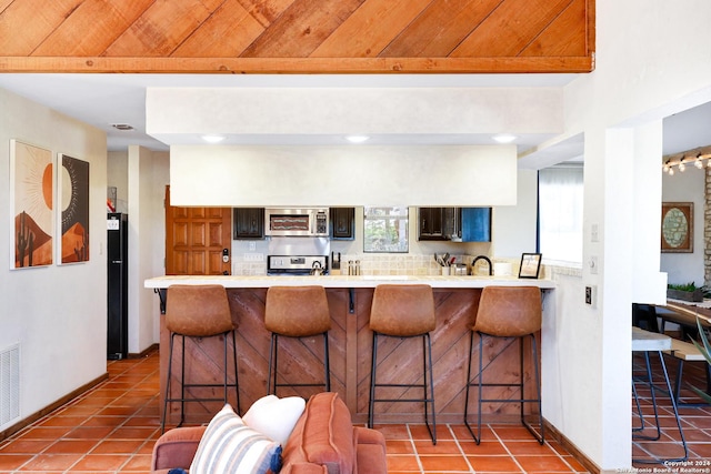 kitchen featuring a breakfast bar area, light countertops, appliances with stainless steel finishes, tile patterned flooring, and a peninsula