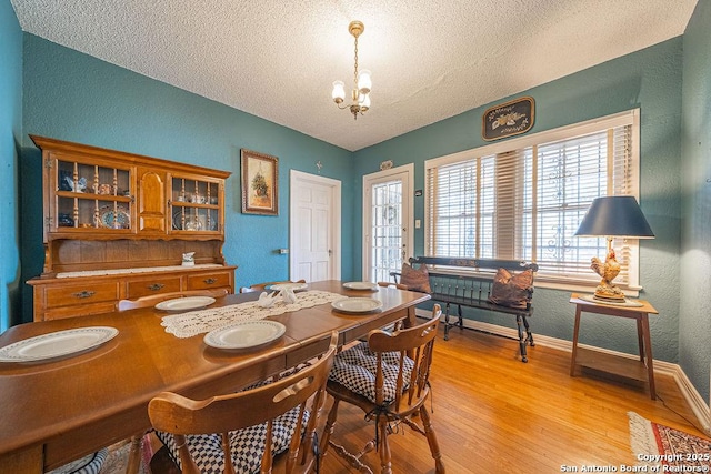 dining space featuring a textured wall, light wood-type flooring, a notable chandelier, and a textured ceiling