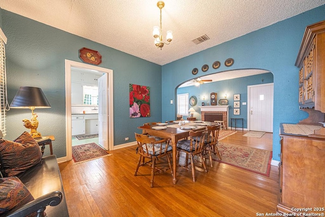 dining area with arched walkways, a textured ceiling, light wood-style flooring, a fireplace, and visible vents