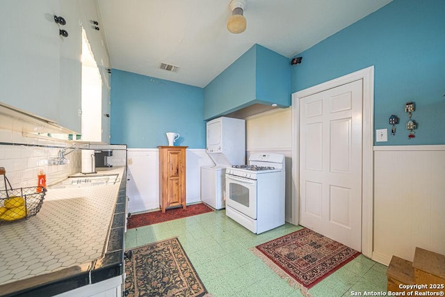 kitchen featuring a wainscoted wall, visible vents, tile counters, light floors, and gas range gas stove