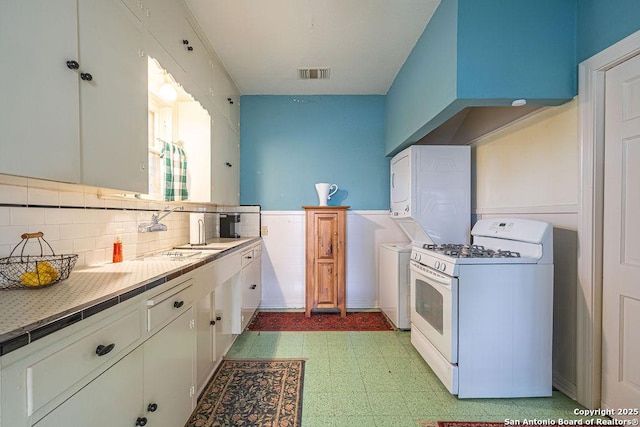 kitchen with white gas stove, light floors, stacked washer and dryer, visible vents, and a sink