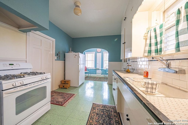 kitchen featuring arched walkways, white appliances, white cabinets, tile counters, and light floors