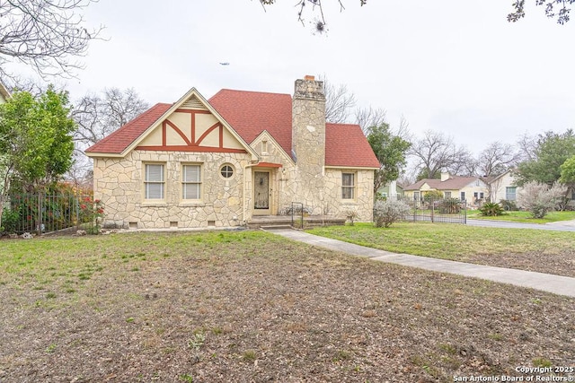 tudor house featuring a shingled roof, a chimney, crawl space, fence, and a front lawn