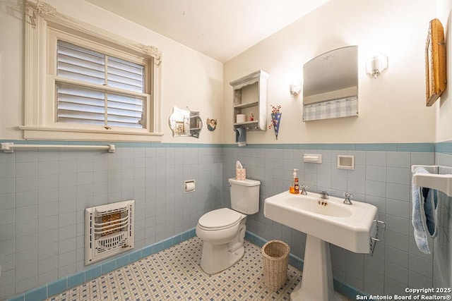 bathroom with heating unit, toilet, tile walls, wainscoting, and tile patterned floors