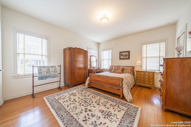 bedroom with multiple windows, light wood-type flooring, and baseboards