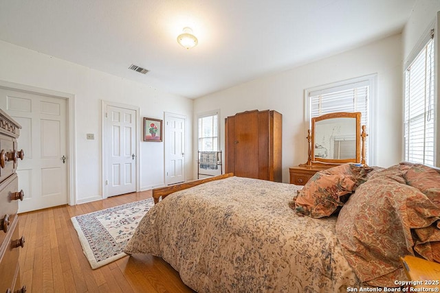 bedroom with light wood-style flooring, multiple windows, visible vents, and two closets