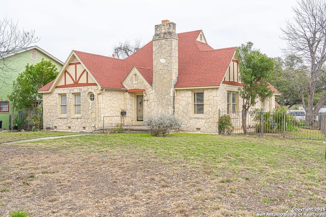 tudor-style house with stone siding, crawl space, a chimney, and fence