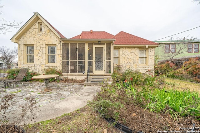 back of house with stone siding, a patio, and a sunroom