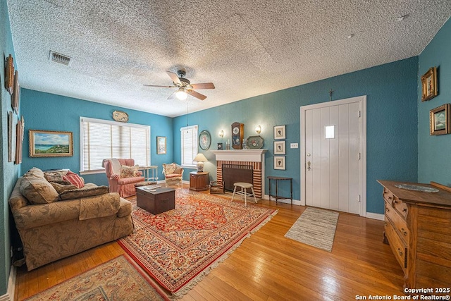 living area featuring ceiling fan, a brick fireplace, wood finished floors, and visible vents