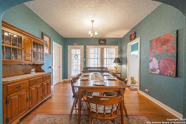 dining room with a chandelier, a textured wall, and light wood finished floors