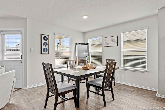 dining area featuring light wood-style floors, baseboards, and a textured ceiling