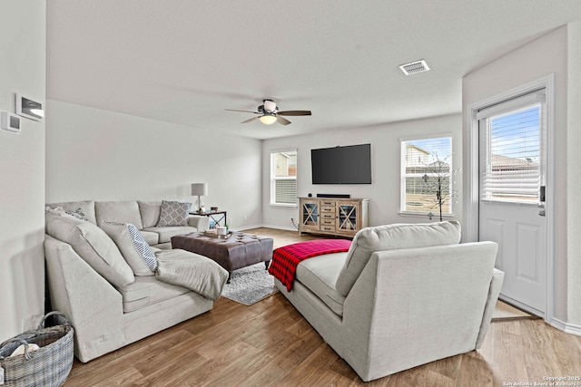 living room with baseboards, light wood-style flooring, visible vents, and a ceiling fan