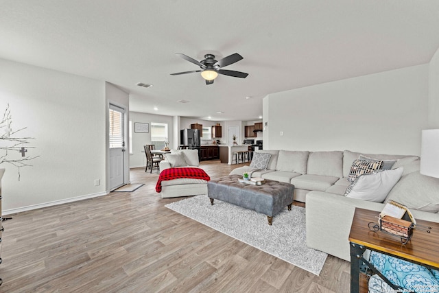 living area with baseboards, ceiling fan, visible vents, and light wood finished floors