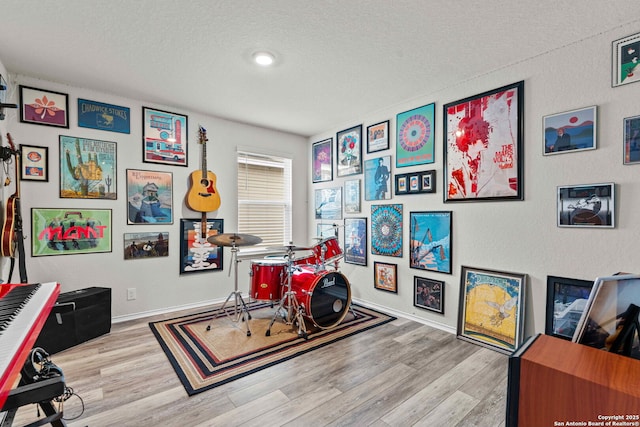 recreation room featuring baseboards, a textured ceiling, and light wood finished floors