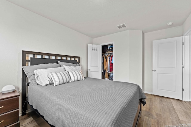 bedroom with baseboards, visible vents, a spacious closet, light wood-style floors, and a closet