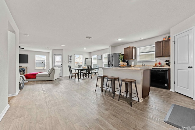 kitchen featuring black dishwasher, light countertops, open floor plan, a center island, and stainless steel fridge