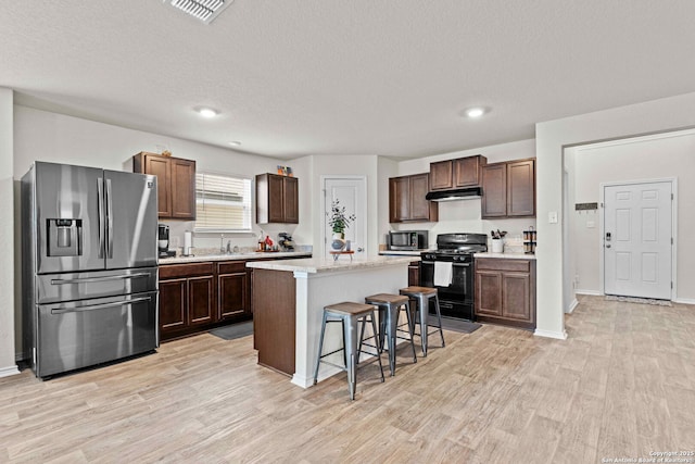 kitchen featuring under cabinet range hood, stainless steel appliances, a kitchen island, a kitchen breakfast bar, and light countertops