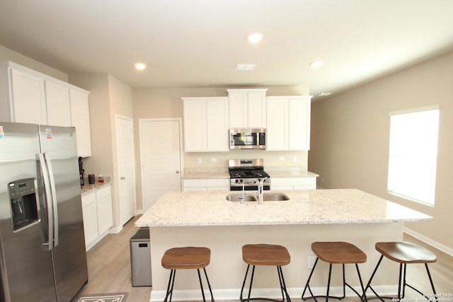 kitchen with stainless steel appliances, white cabinetry, a center island with sink, and light stone counters