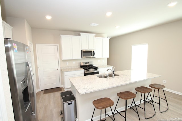 kitchen featuring light stone counters, stainless steel appliances, a sink, white cabinets, and an island with sink