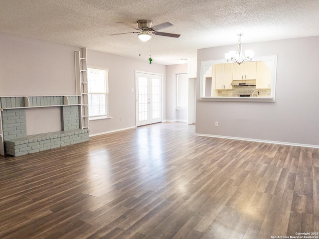 unfurnished living room with ceiling fan with notable chandelier, baseboards, french doors, a brick fireplace, and dark wood finished floors