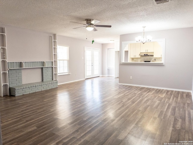 unfurnished living room with dark wood finished floors, a textured ceiling, french doors, a brick fireplace, and ceiling fan with notable chandelier