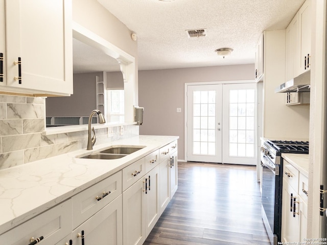 kitchen featuring light stone counters, white cabinetry, a sink, stainless steel gas range, and under cabinet range hood