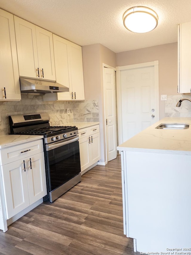 kitchen with dark wood-style flooring, white cabinets, stainless steel range with gas stovetop, a sink, and under cabinet range hood