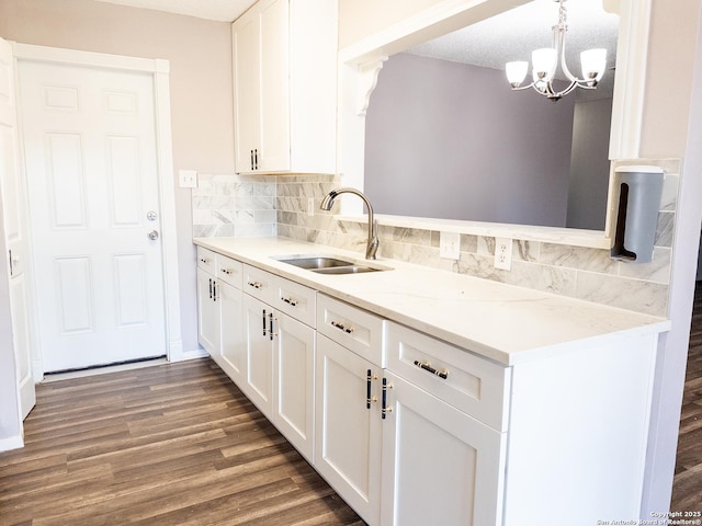 kitchen with light stone counters, a sink, white cabinets, hanging light fixtures, and dark wood-style floors