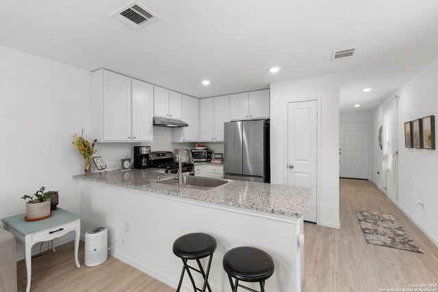 kitchen featuring under cabinet range hood, a peninsula, visible vents, white cabinetry, and appliances with stainless steel finishes