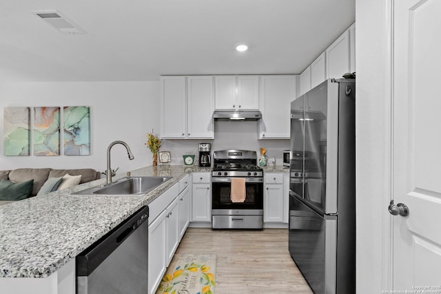 kitchen with under cabinet range hood, stainless steel appliances, a peninsula, a sink, and visible vents