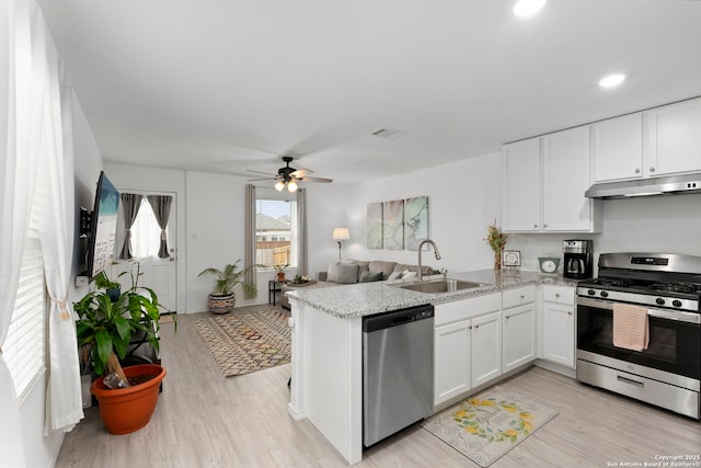 kitchen featuring appliances with stainless steel finishes, open floor plan, under cabinet range hood, white cabinetry, and a sink