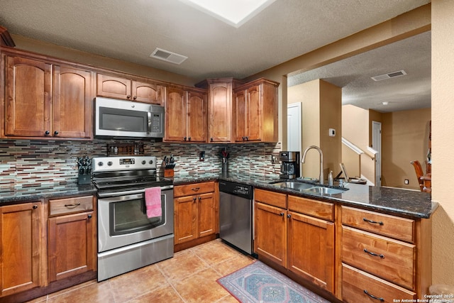 kitchen featuring stainless steel appliances, a sink, visible vents, brown cabinets, and dark stone counters