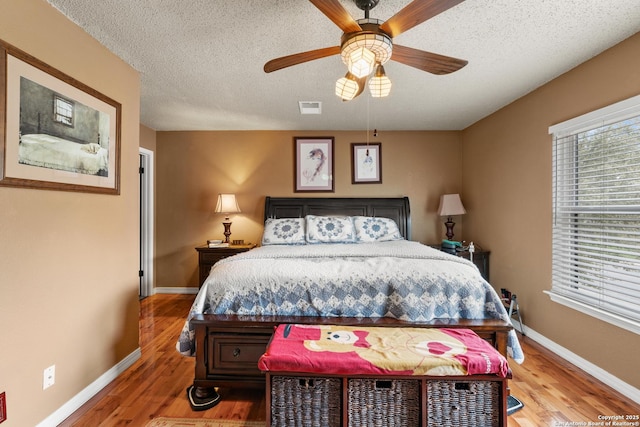 bedroom with a textured ceiling, wood finished floors, visible vents, and baseboards