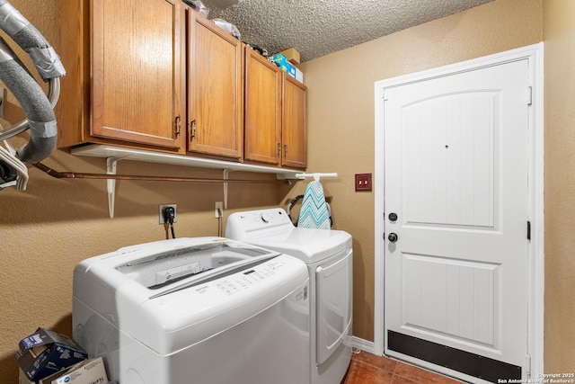 washroom with a textured ceiling, dark tile patterned flooring, washer and clothes dryer, and cabinet space