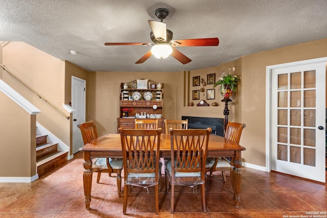 dining space featuring ceiling fan, a fireplace, a textured ceiling, and stairs