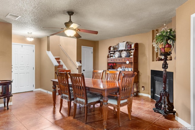 tiled dining room with baseboards, visible vents, ceiling fan, stairway, and a fireplace