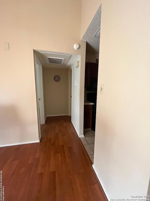 hallway with baseboards, visible vents, and wood finished floors