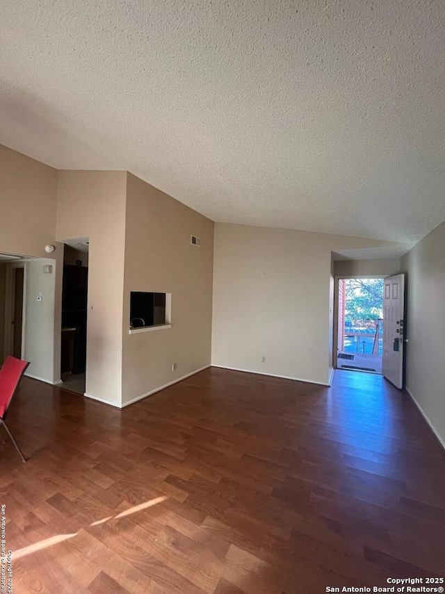 empty room featuring a textured ceiling, visible vents, vaulted ceiling, and wood finished floors